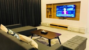 A modern living room with a large flat-screen TV mounted on a wall, a dark-colored sofa, a wooden coffee table, and a small side table. - Araucaria Residence (Huxi)