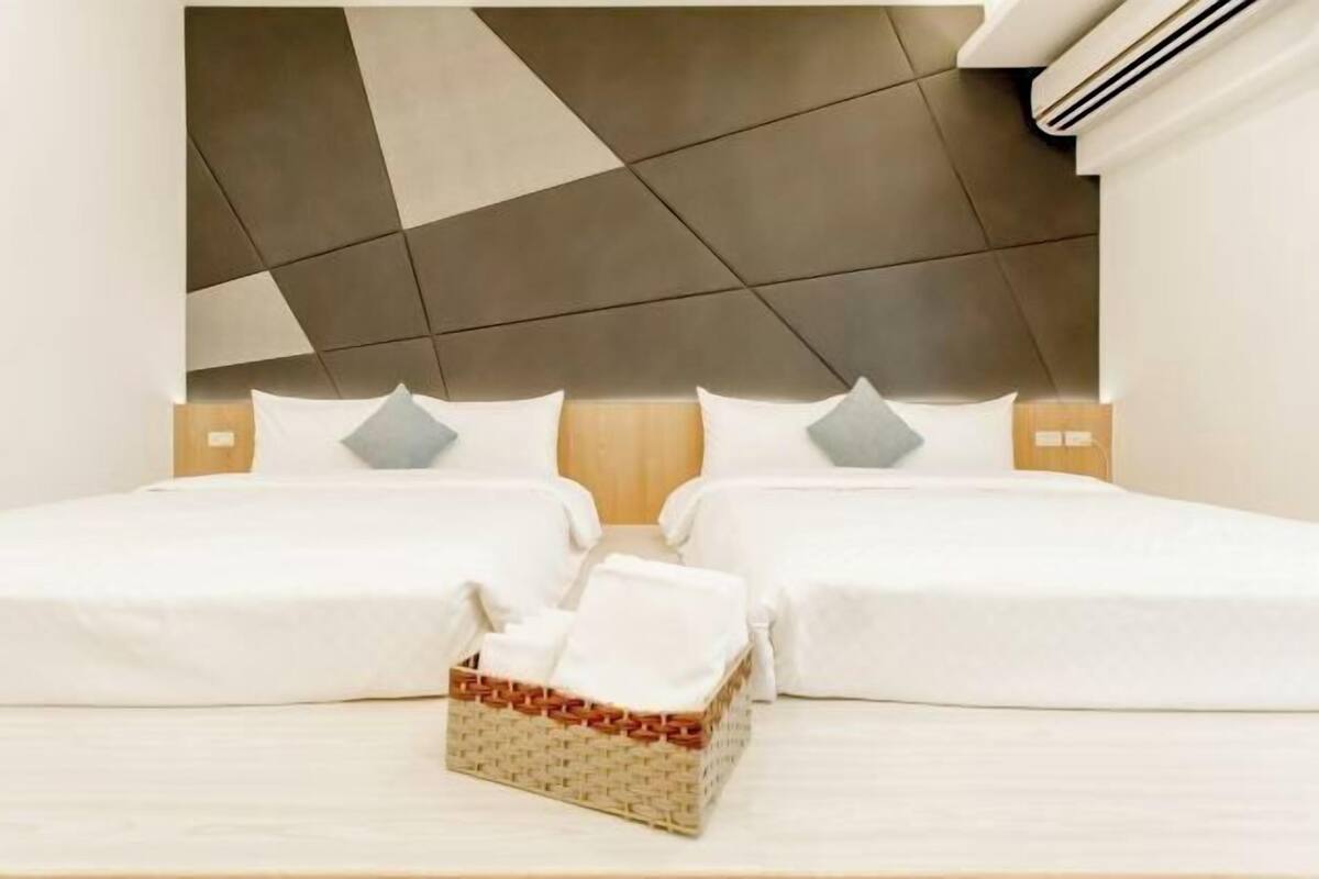 Habitación de hotel con un cabecero moderno, dos camas, una pequeña cesta de mimbre y una mesita de noche de madera.