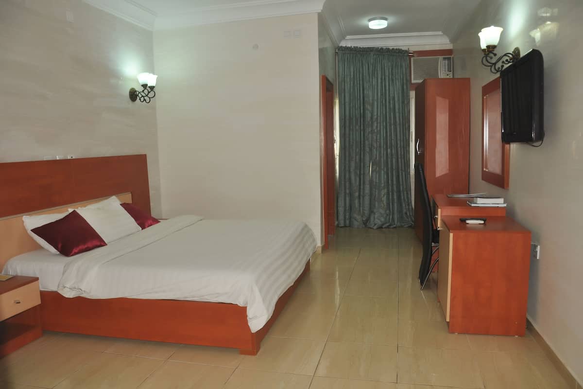A hotel room with a bed, a wooden nightstand, a desk, a mirror, and a curtain.