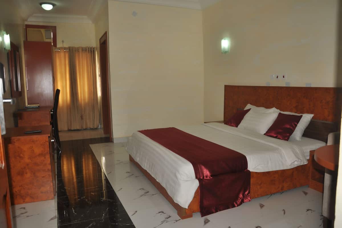 A hotel room with a double bed, a desk, a chair, and a bathroom visible in the background.