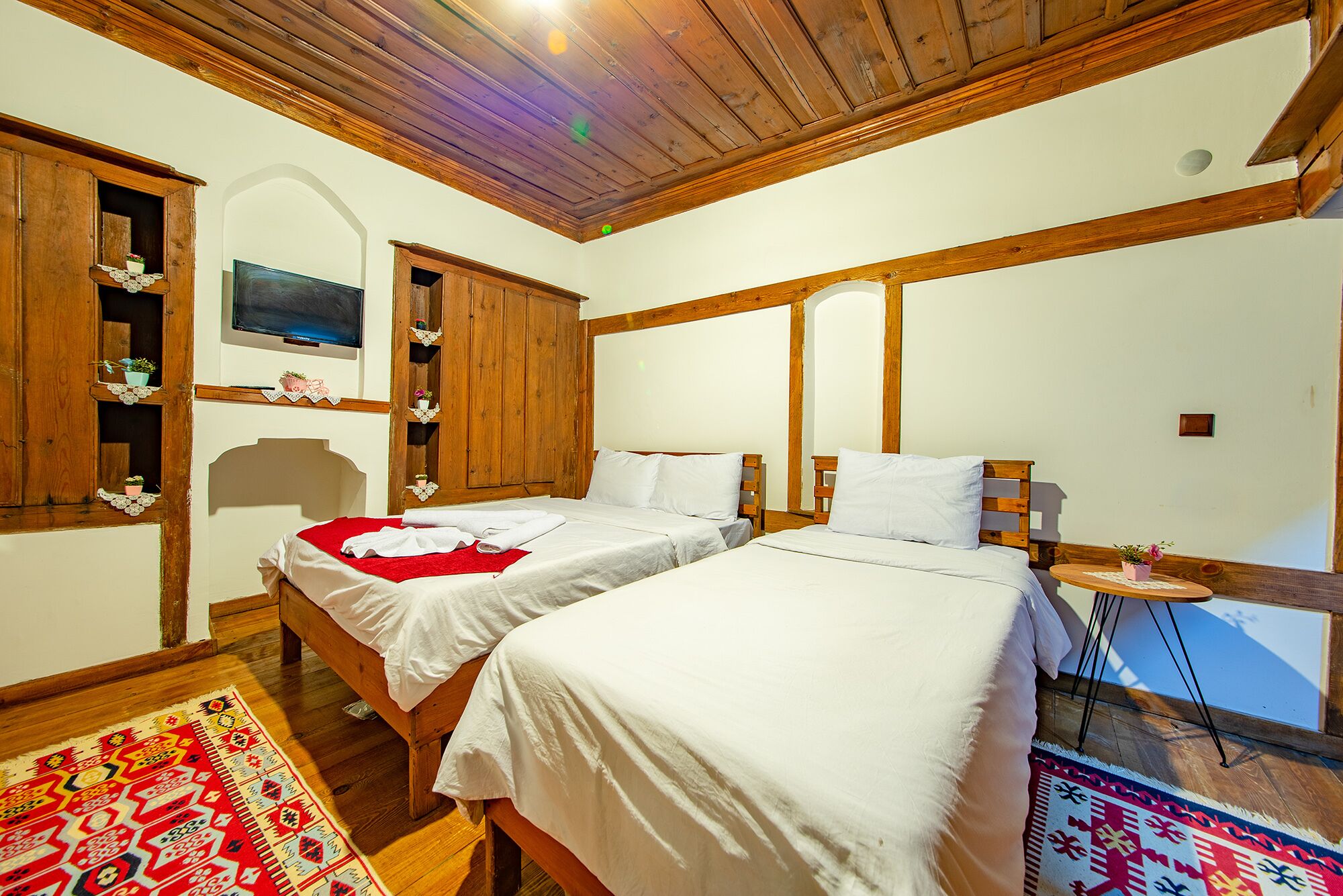 Una habitación con dos camas, vigas de madera, un televisor y una pequeña mesa con una planta.