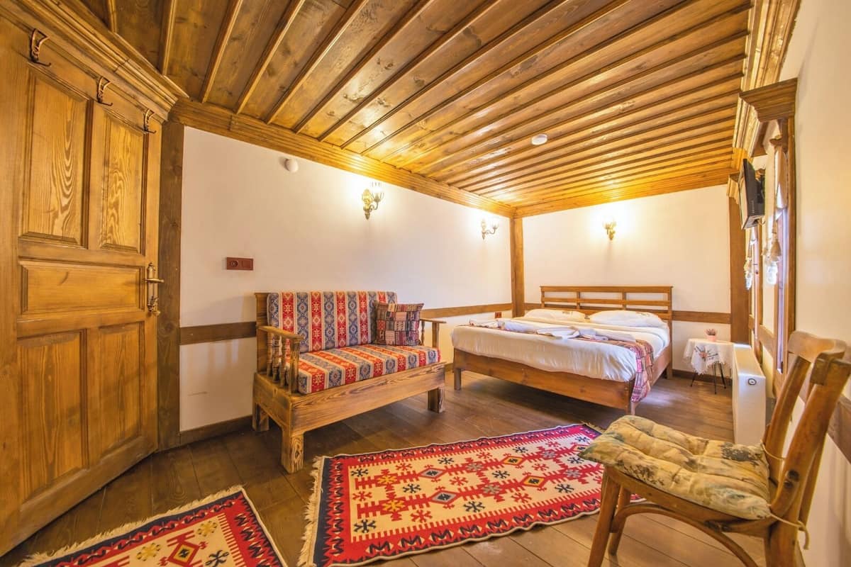 A cozy room with wooden ceiling beams, a sofa with patterned cushions, a bed, and a chair.