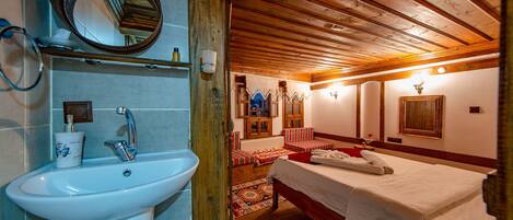 Un dormitorio con techo de madera, una cama, una mesita de noche, un espejo y un baño con lavabo y toallero.