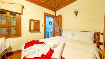 A hotel room with a wooden ceiling, a bed with white linens, a red throw blanket, and a wooden wardrobe.