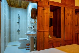 Un baño con inodoro blanco, lavabo y ducha. Hay un armario de madera con un espejo sobre el lavabo.
