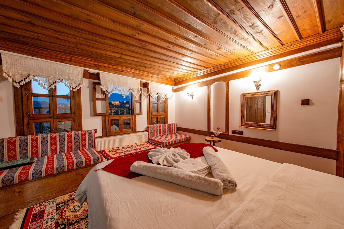 A cozy room with a wooden ceiling, a large bed with white linens, a red sofa, and a view of a mountain at dusk.
