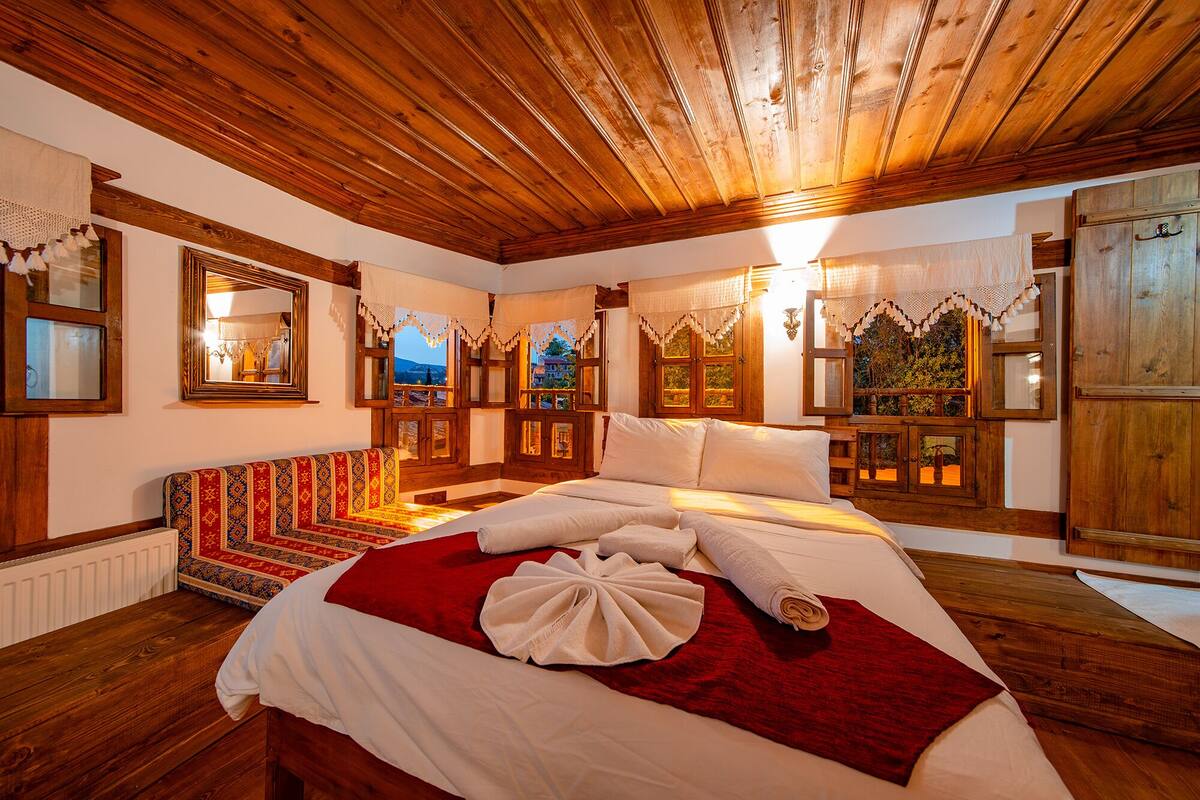 A traditional wooden room with a bed, a patterned sofa, and a view of the outdoors through windows.