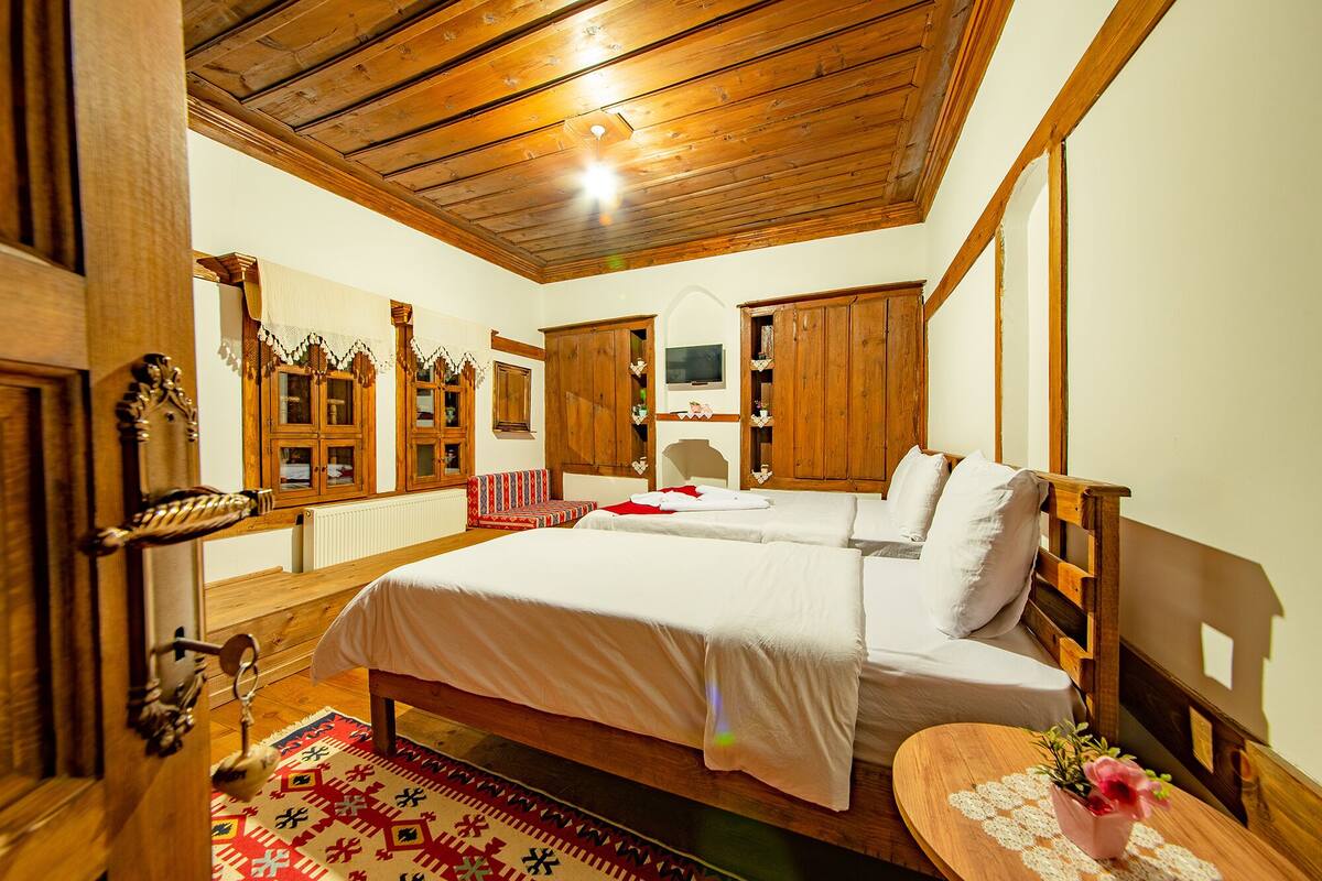 A traditional room with a wooden ceiling, a bed with white linens, a small round table with a vase, and wooden cabinets.