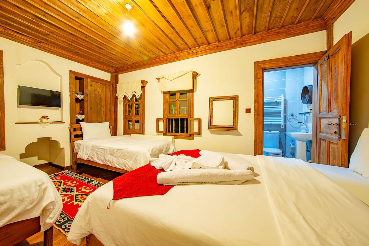 A hotel room with two beds, wooden ceiling, a TV, and a bathroom visible through an open door.