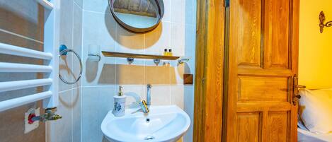 Un baño con lavamanos blanco, un espejo, toallero y puerta de madera.