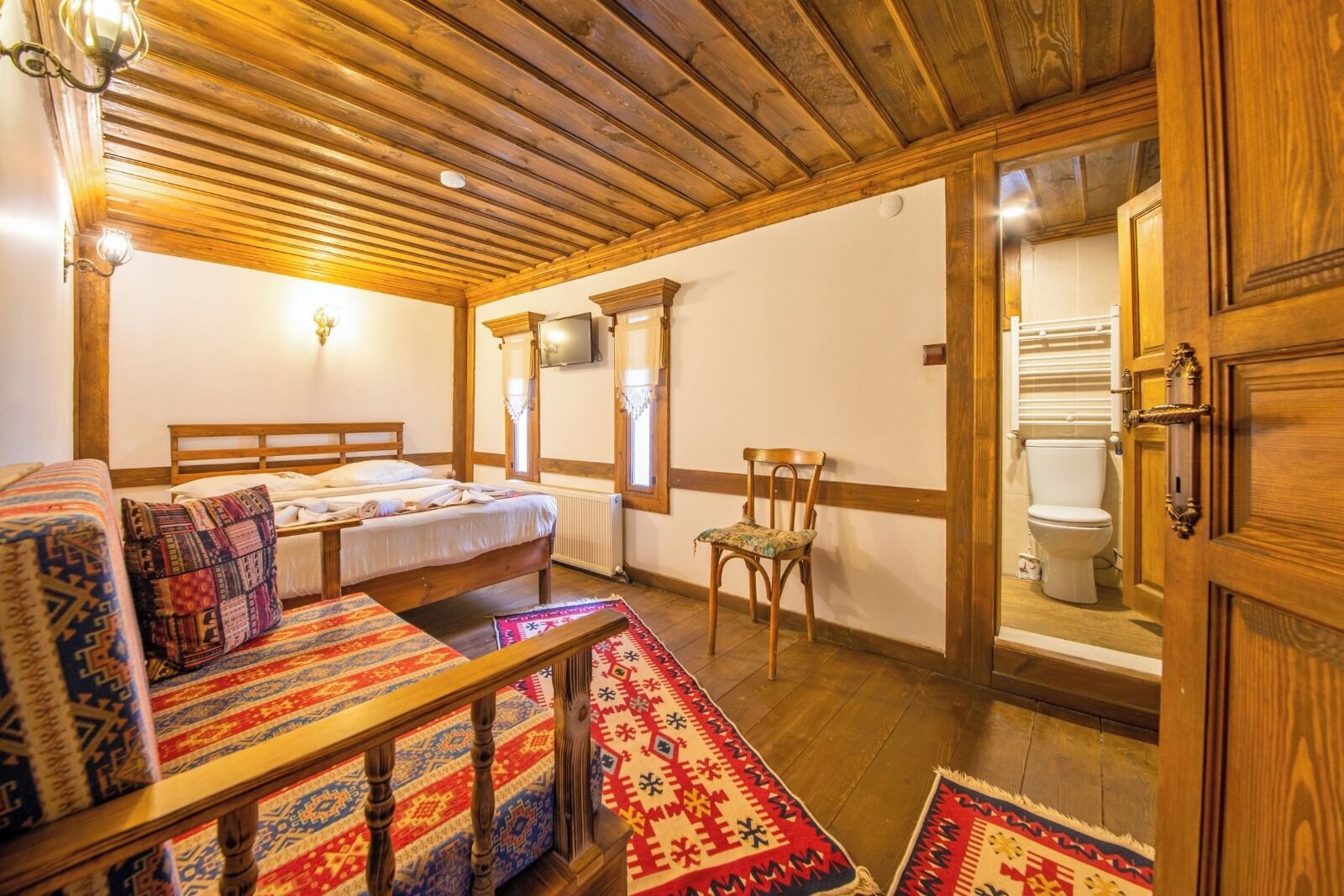 A cozy room with a bed, a chair, a table, and a bathroom visible through an open door.