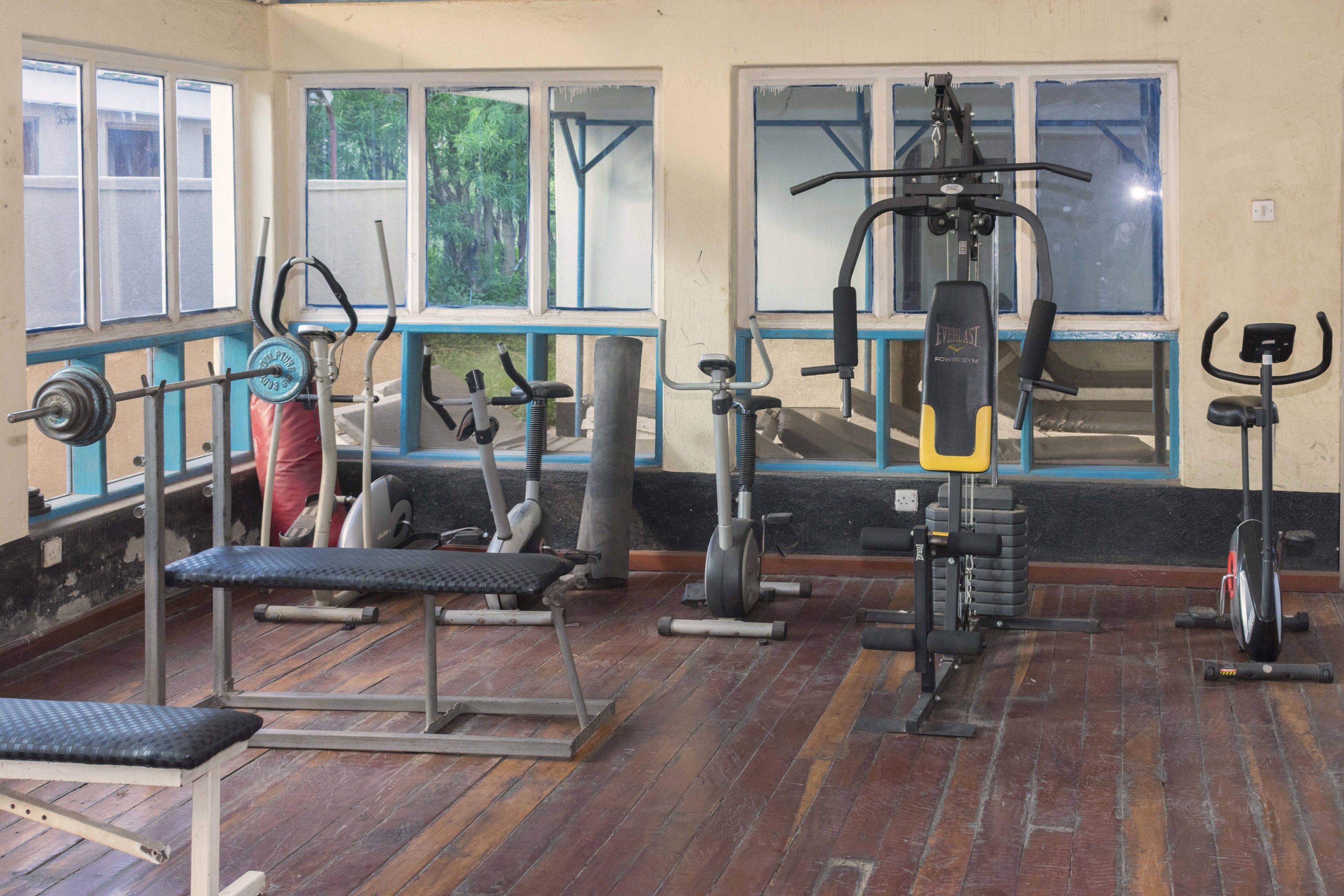Un gimnasio con diferentes máquinas de ejercicio, ventanas amplias y piso de madera.