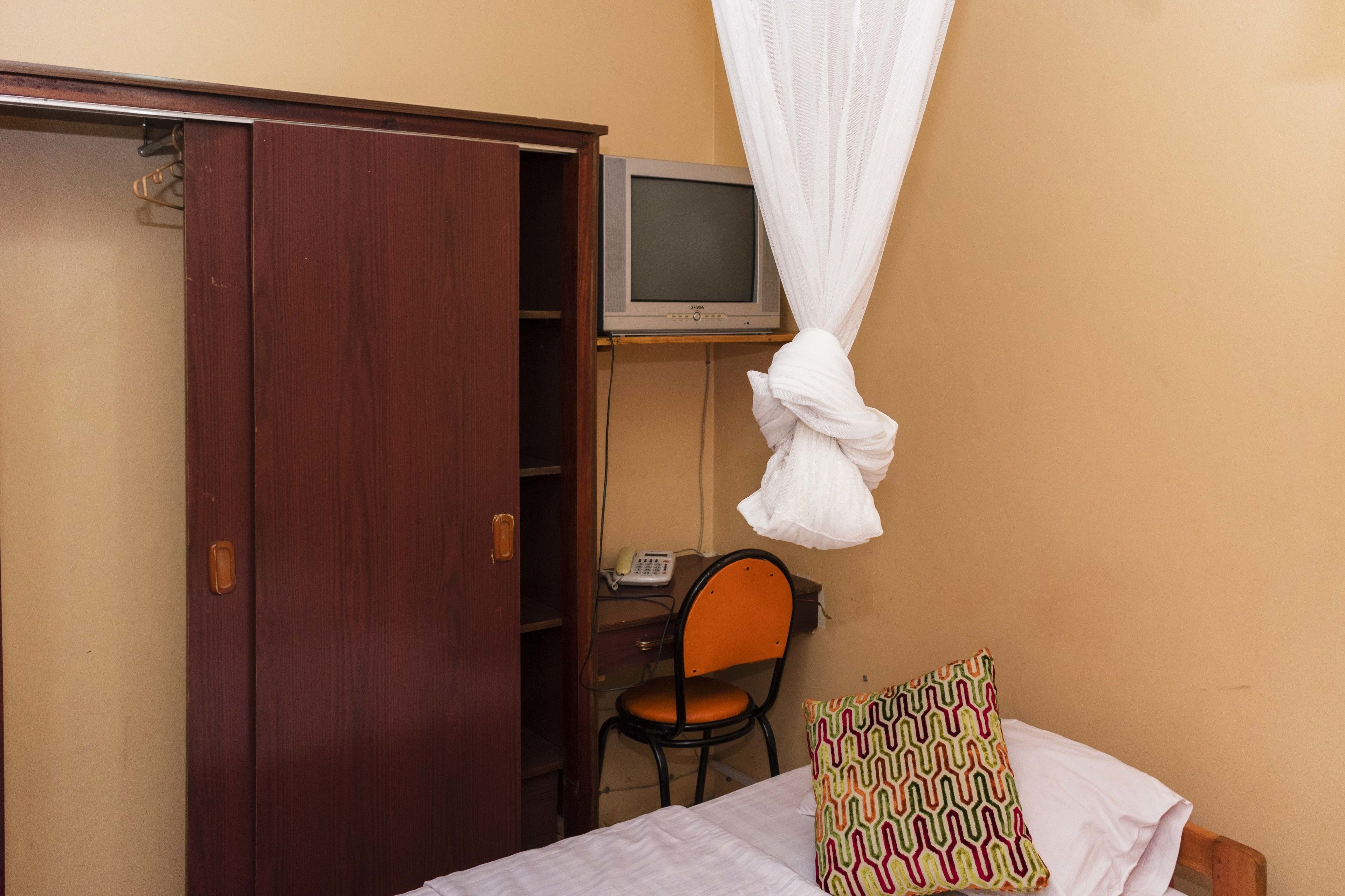 A bedroom with a bed, a chair, a desk with a computer, and a television.