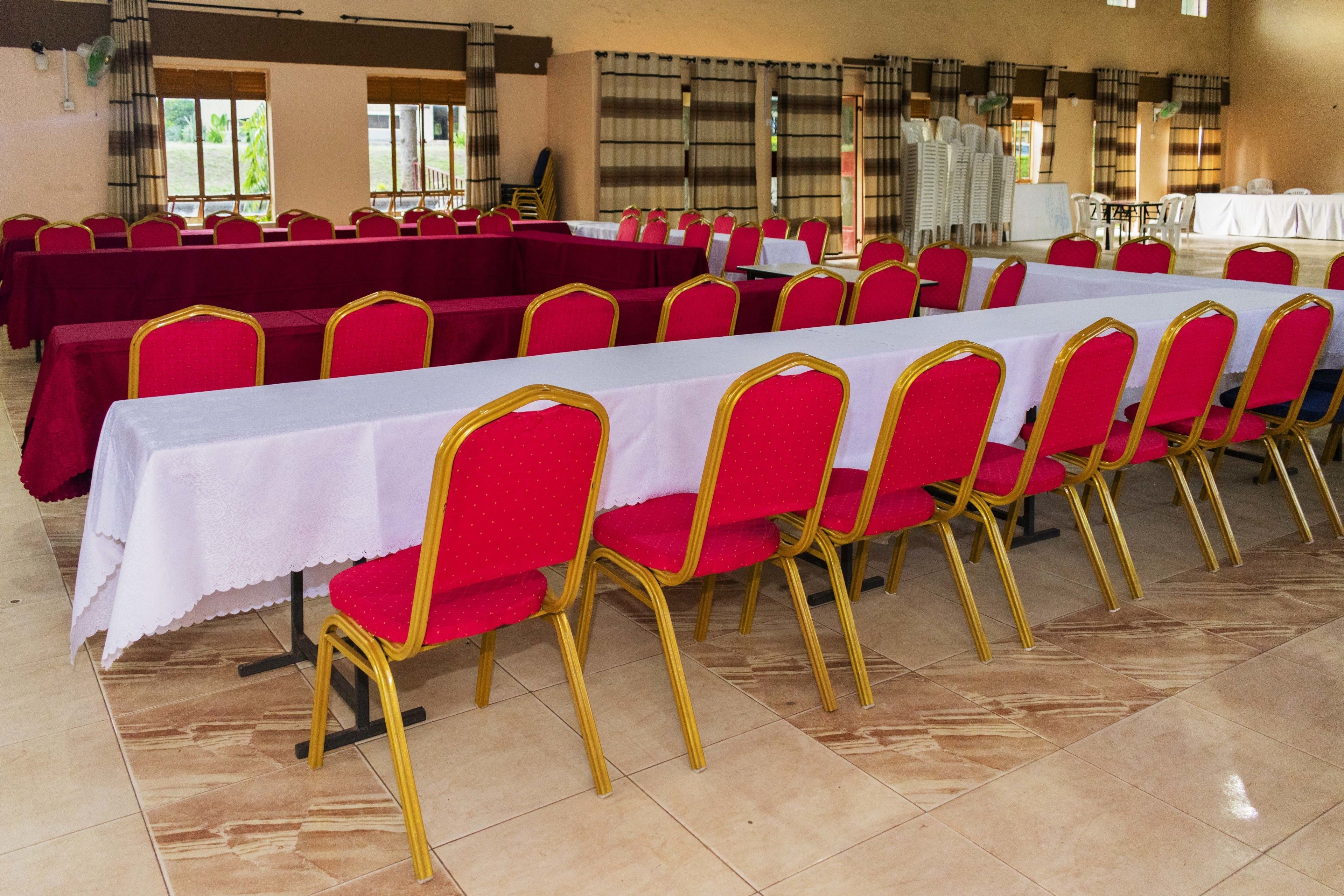 A conference room with rows of tables and chairs, large windows, and a tiled floor.