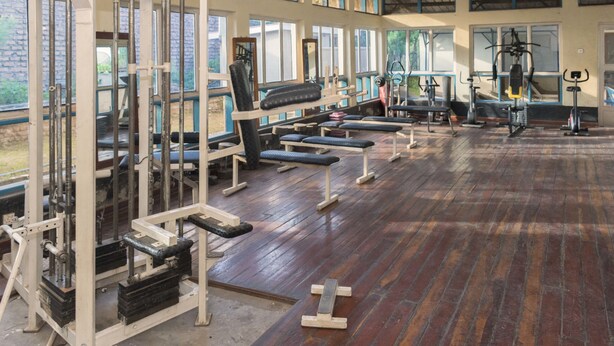 A gym with various exercise equipment, large windows, and a wooden floor. - Rwenzori International Hotel (Kasese)
