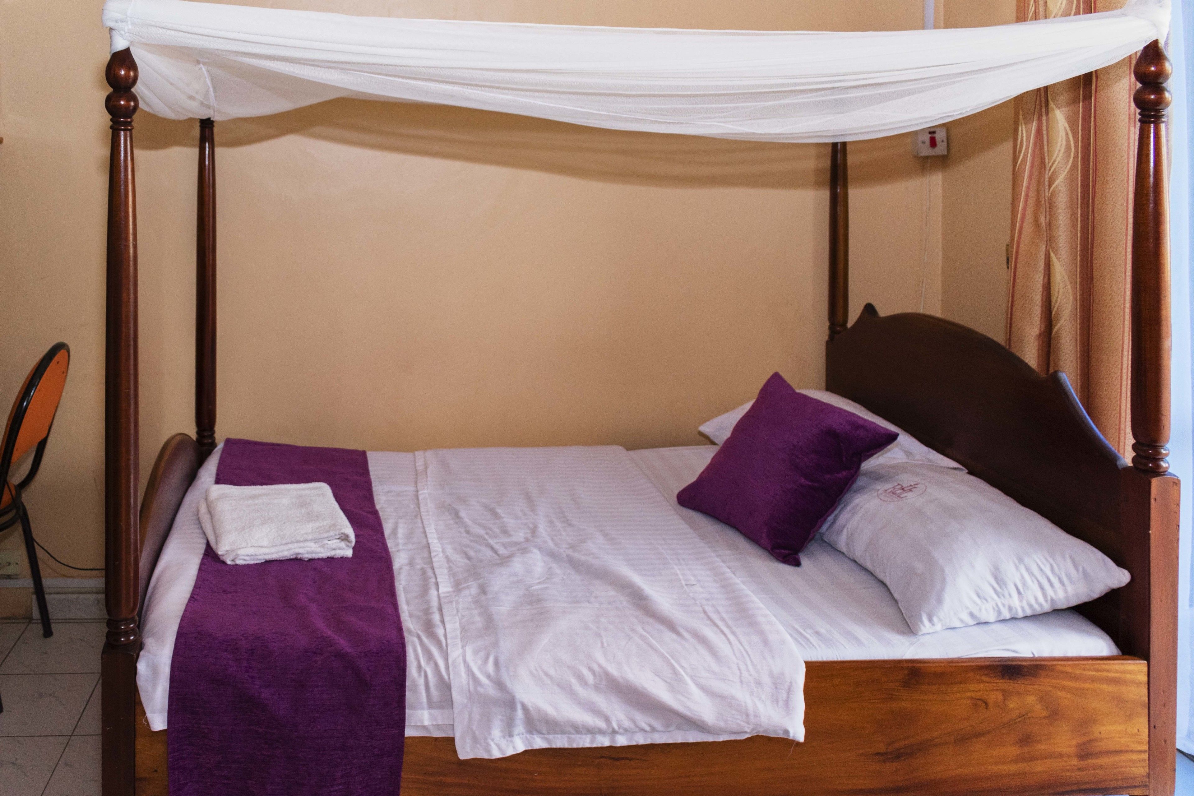 Een keurig opgemaakt bed met een baldakijn, een paarse deken en twee kussens.