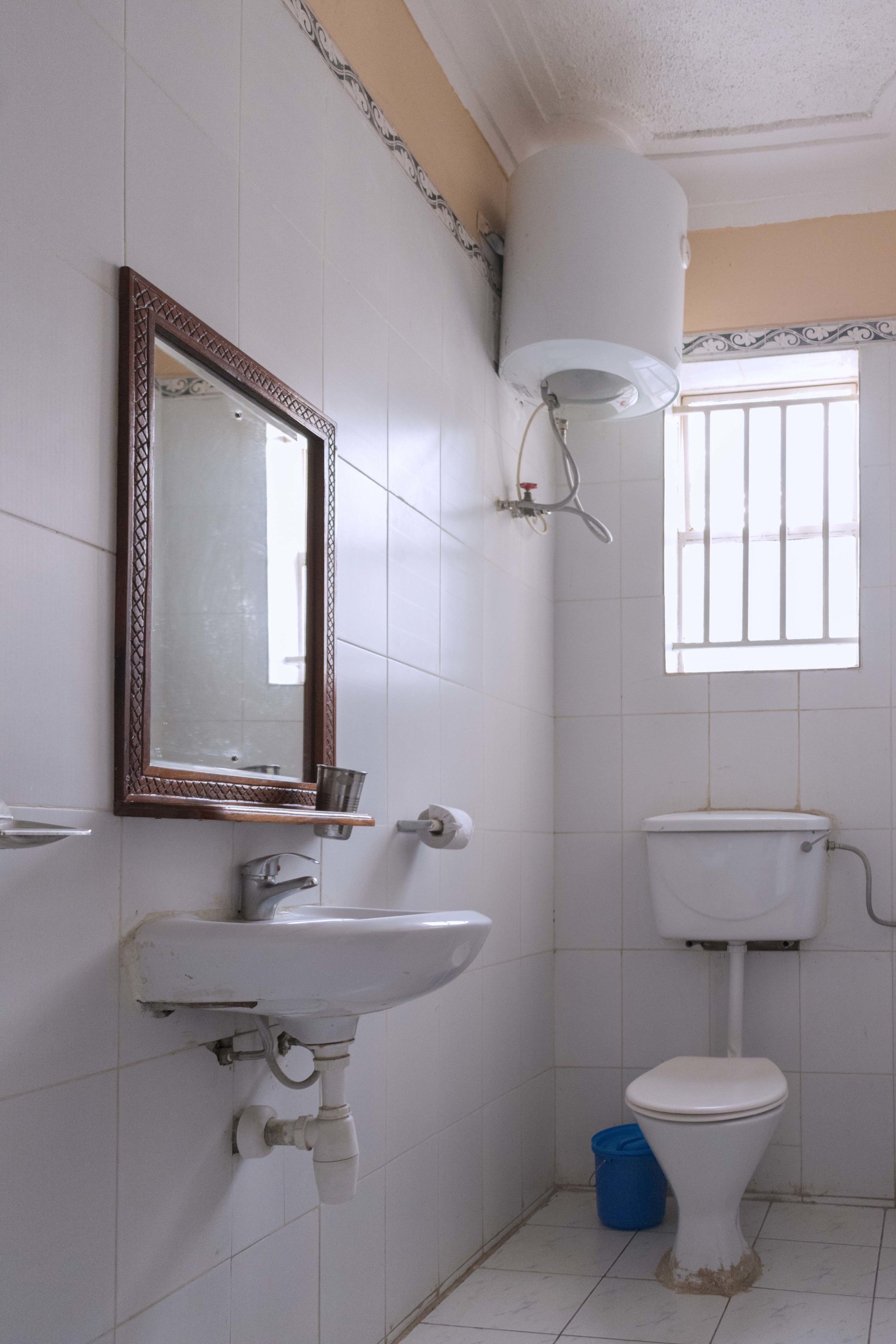 A bathroom with a sink, mirror, toilet, and a window.