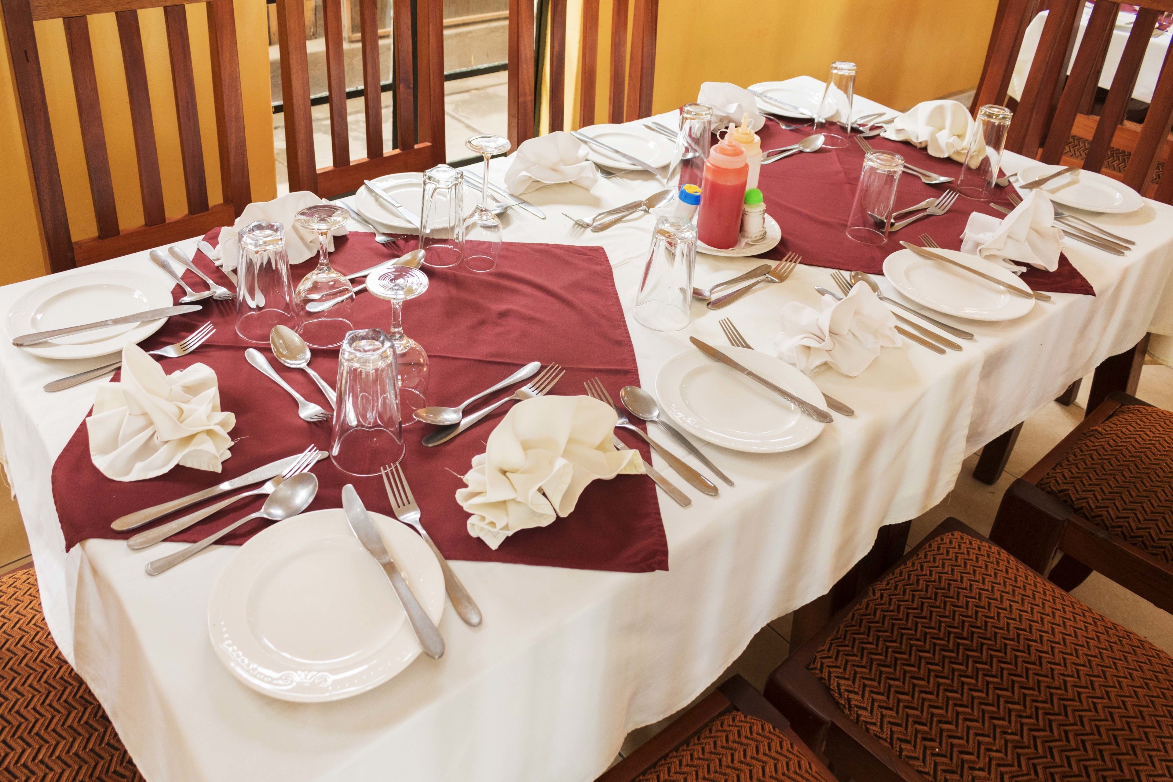 Une table à manger dressée pour un repas, avec de l’assiette blanche, des couverts en argent et des serviettes rouges.