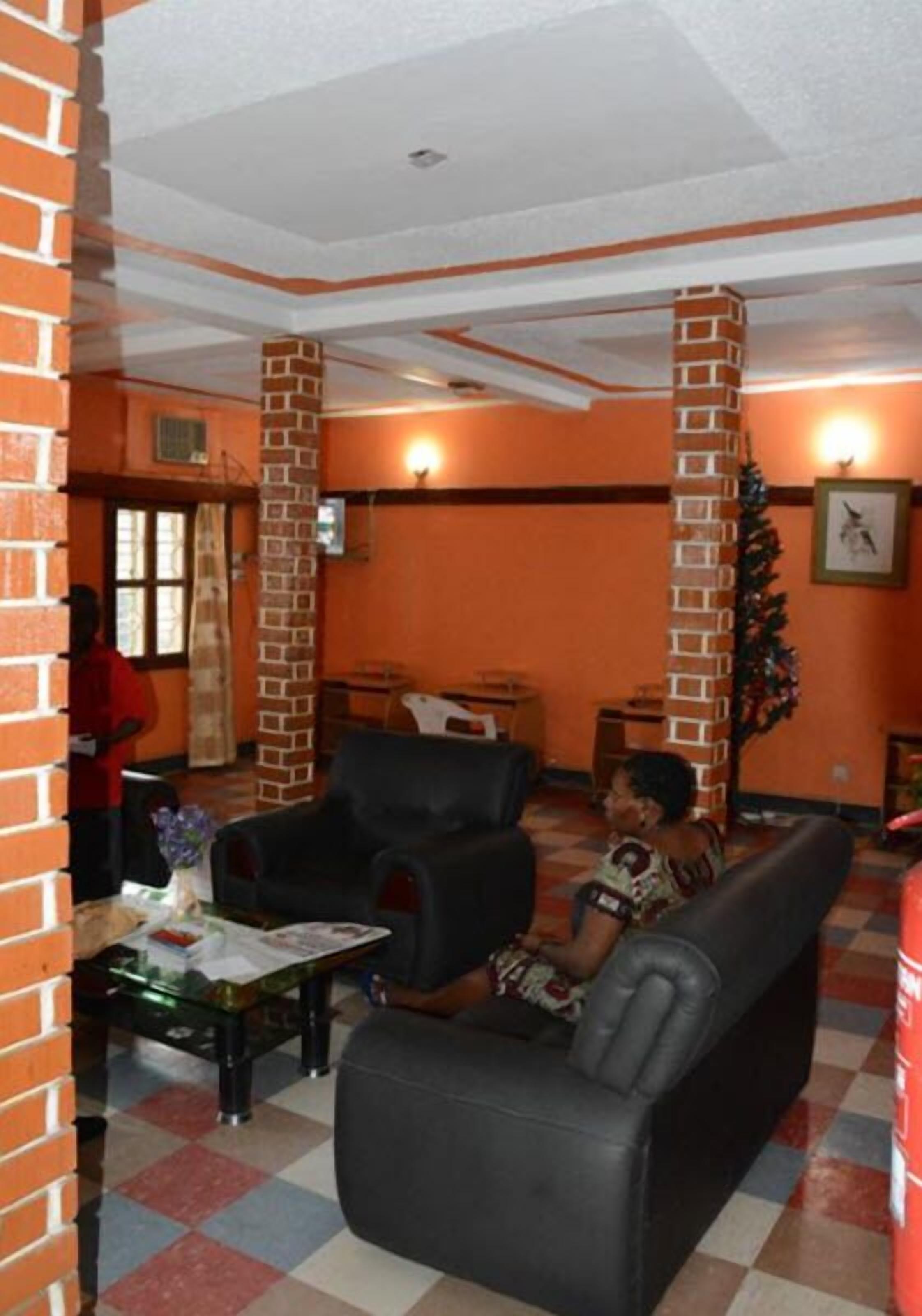 A lobby with a checkered floor, a black leather sofa, a glass coffee table, and a brick pillar.