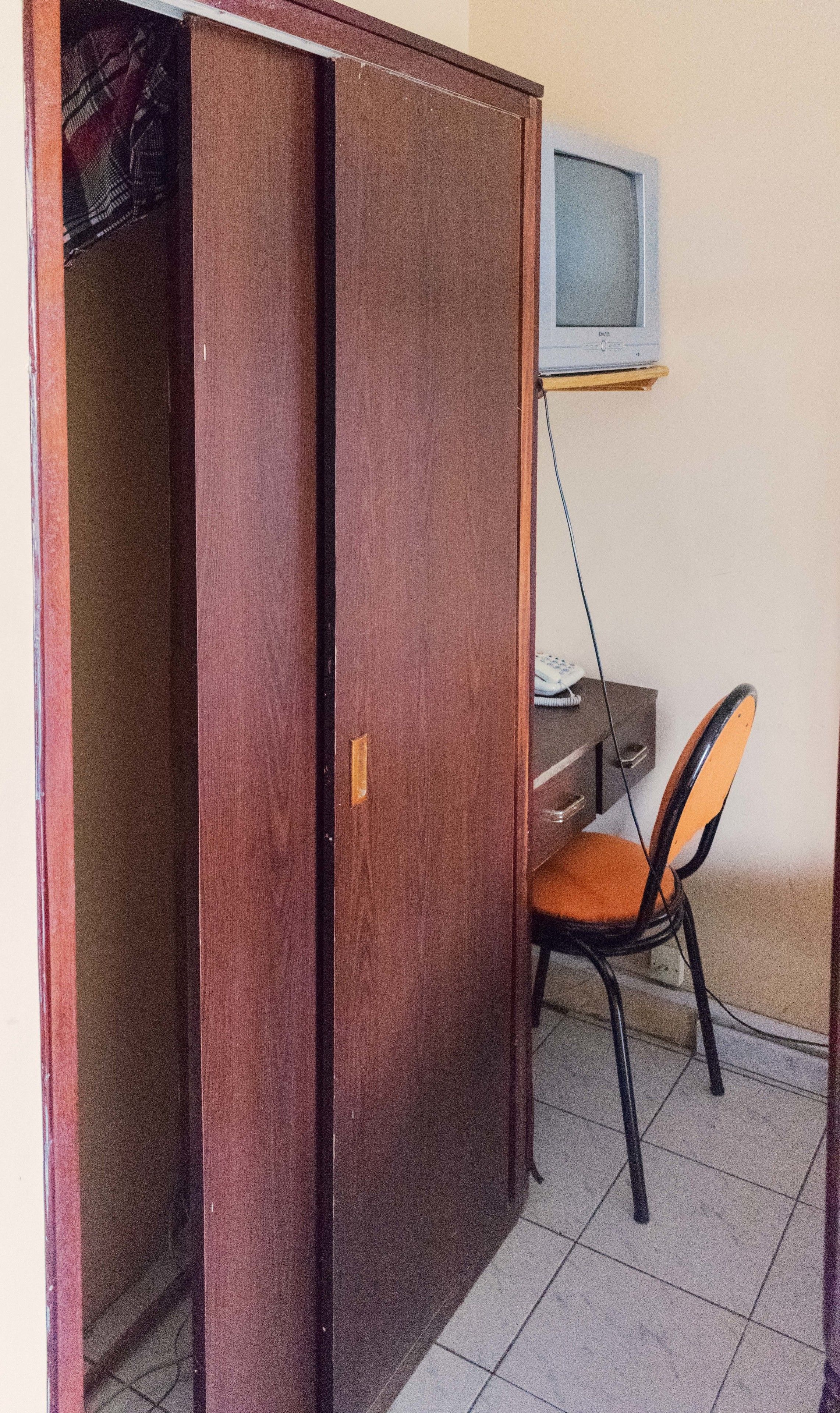 Una habitación con un armario de madera, un escritorio con una silla y un televisor sobre un mueble.