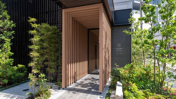 Une entrée d’hôtel moderne, avec un design à lattes de bois, un chemin en pierre et une végétation luxuriante.