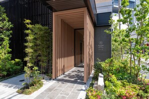 Une entrée d’hôtel moderne, avec un design à lattes de bois, un chemin en pierre et une végétation luxuriante.