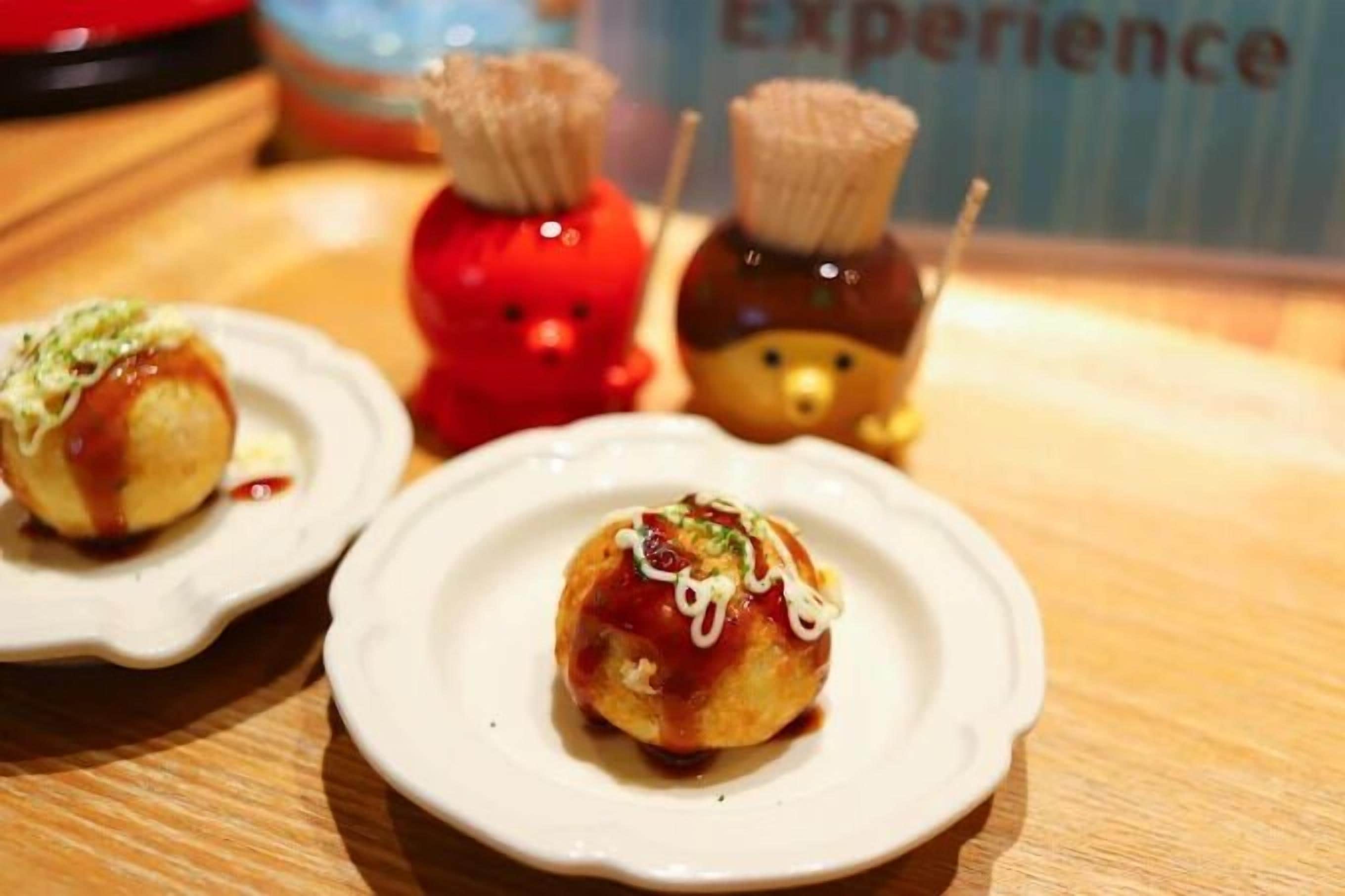 Three small plates with food items, a red decorative object, and a bear-shaped item on a wooden surface.