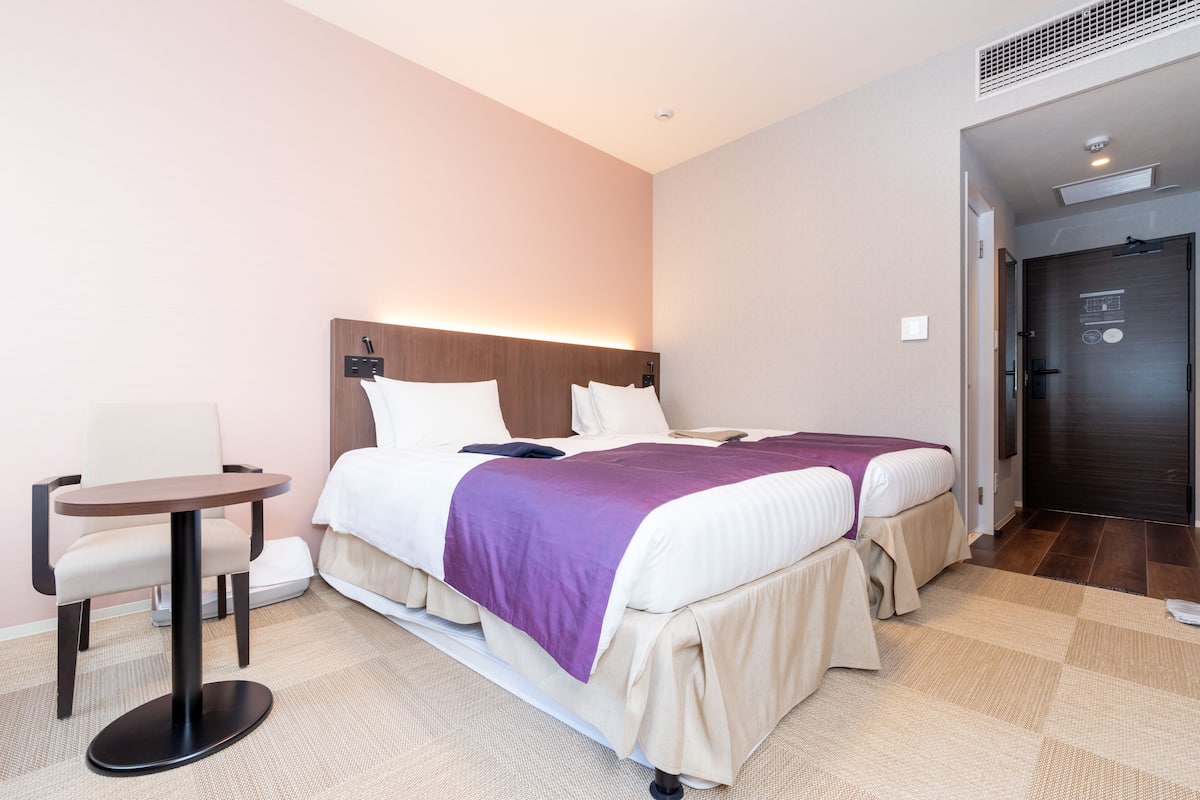 Ein Hotelzimmer mit zwei Betten, einem kleinen runden Tisch und einem Stuhl.