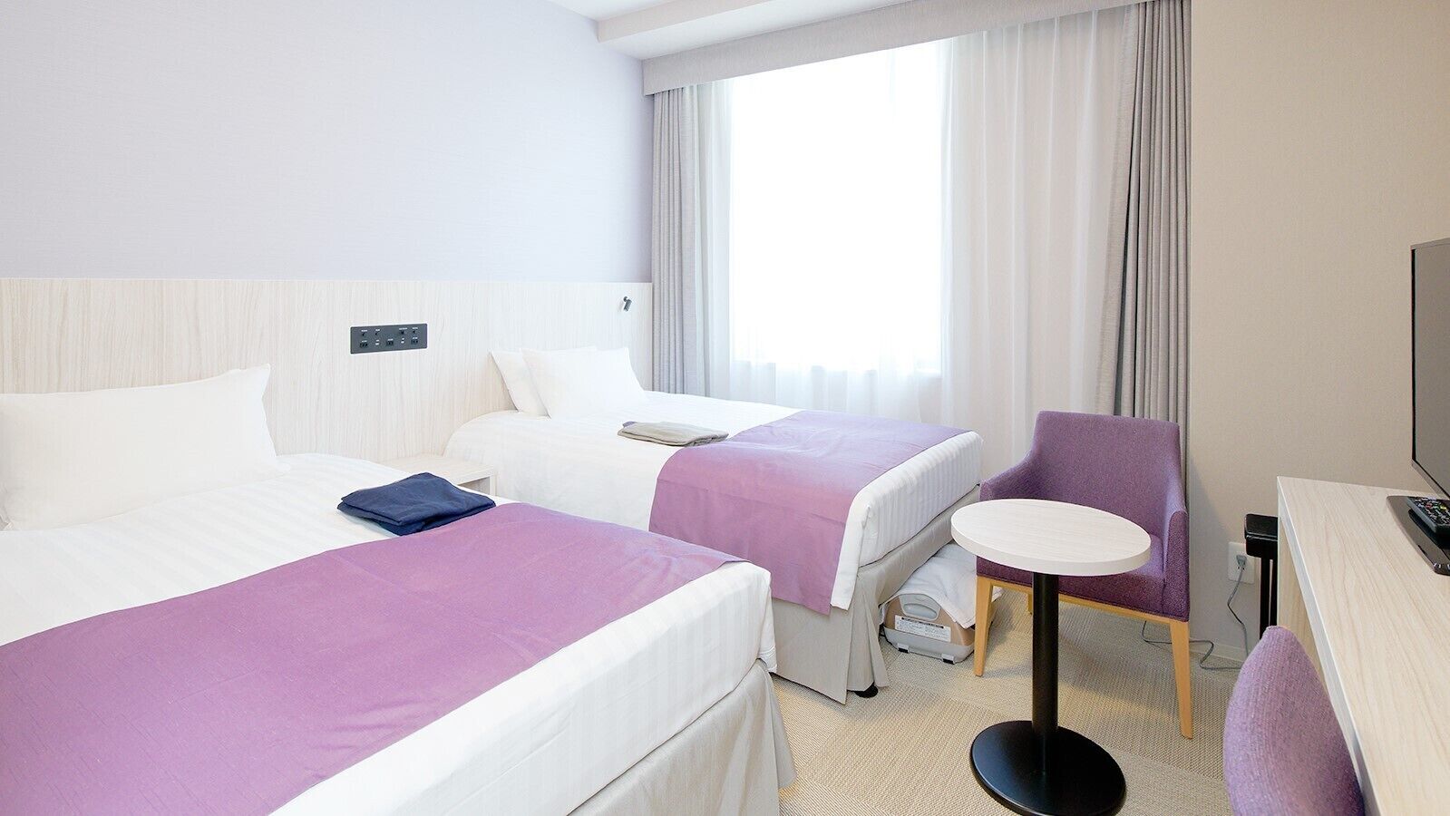 Une chambre d’hôtel avec deux lits, un bureau, une chaise, une télévision et une fenêtre avec des rideaux.
