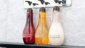 Three bottles of body soap, shampoo, and conditioner on a shelf.