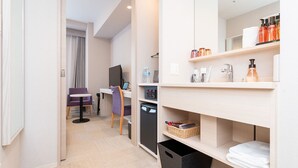 Une chambre d’hôtel équipée d’un bureau, d’une chaise, d’un ordinateur et d’une salle de bain avec des étagères et des articles de toilette.