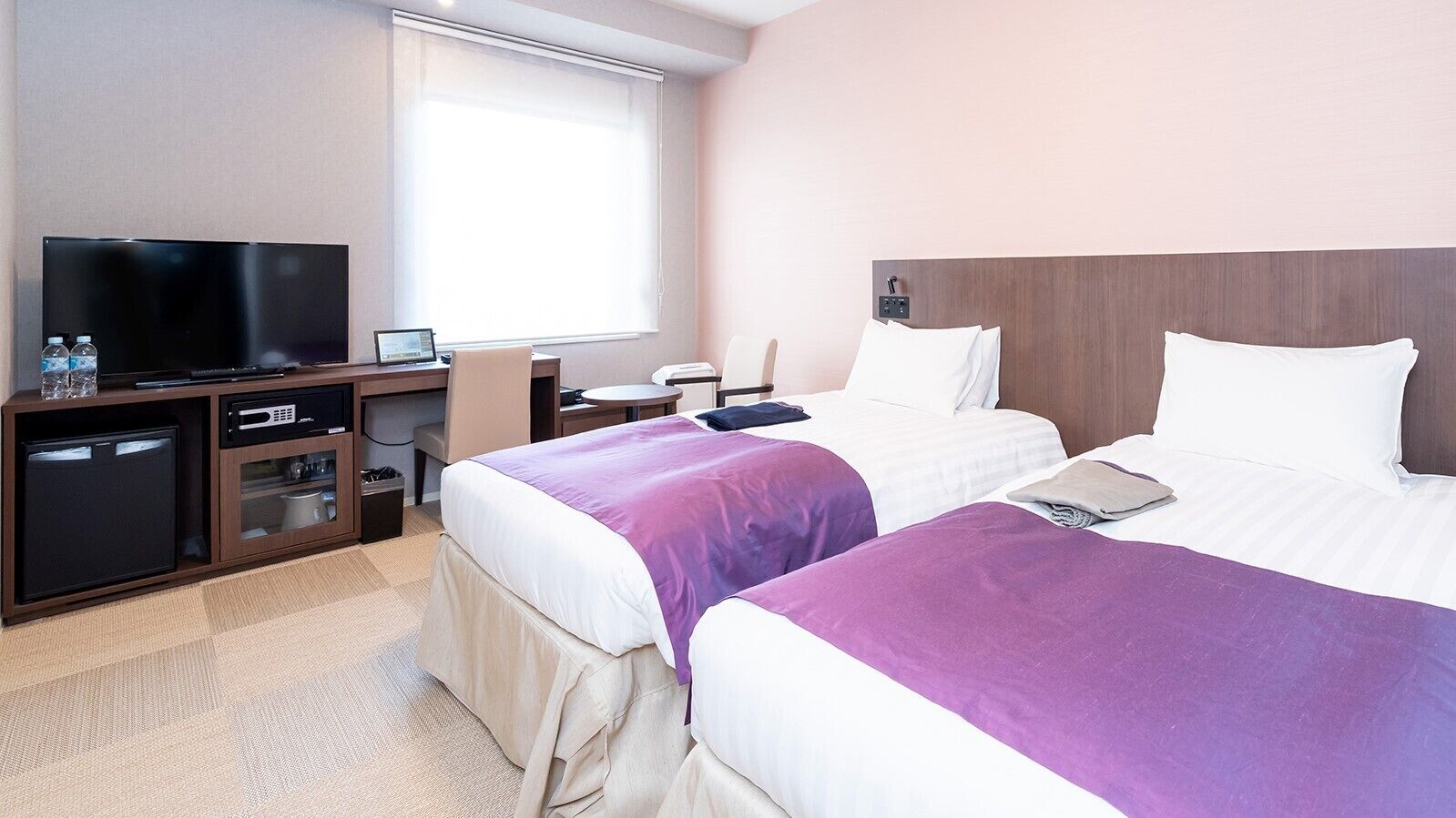 Une chambre d’hôtel avec deux lits, une télévision, un bureau et une petite kitchenette.