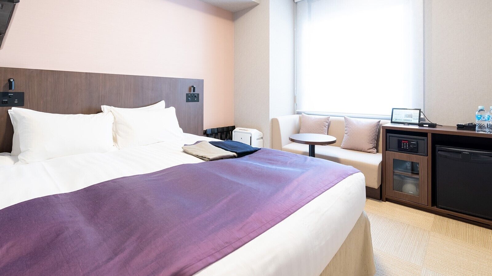 Une chambre d’hôtel équipée d’un lit, d’un bureau, d’une chaise, d’une petite table, d’un four à micro-ondes et d’un mini-réfrigérateur.