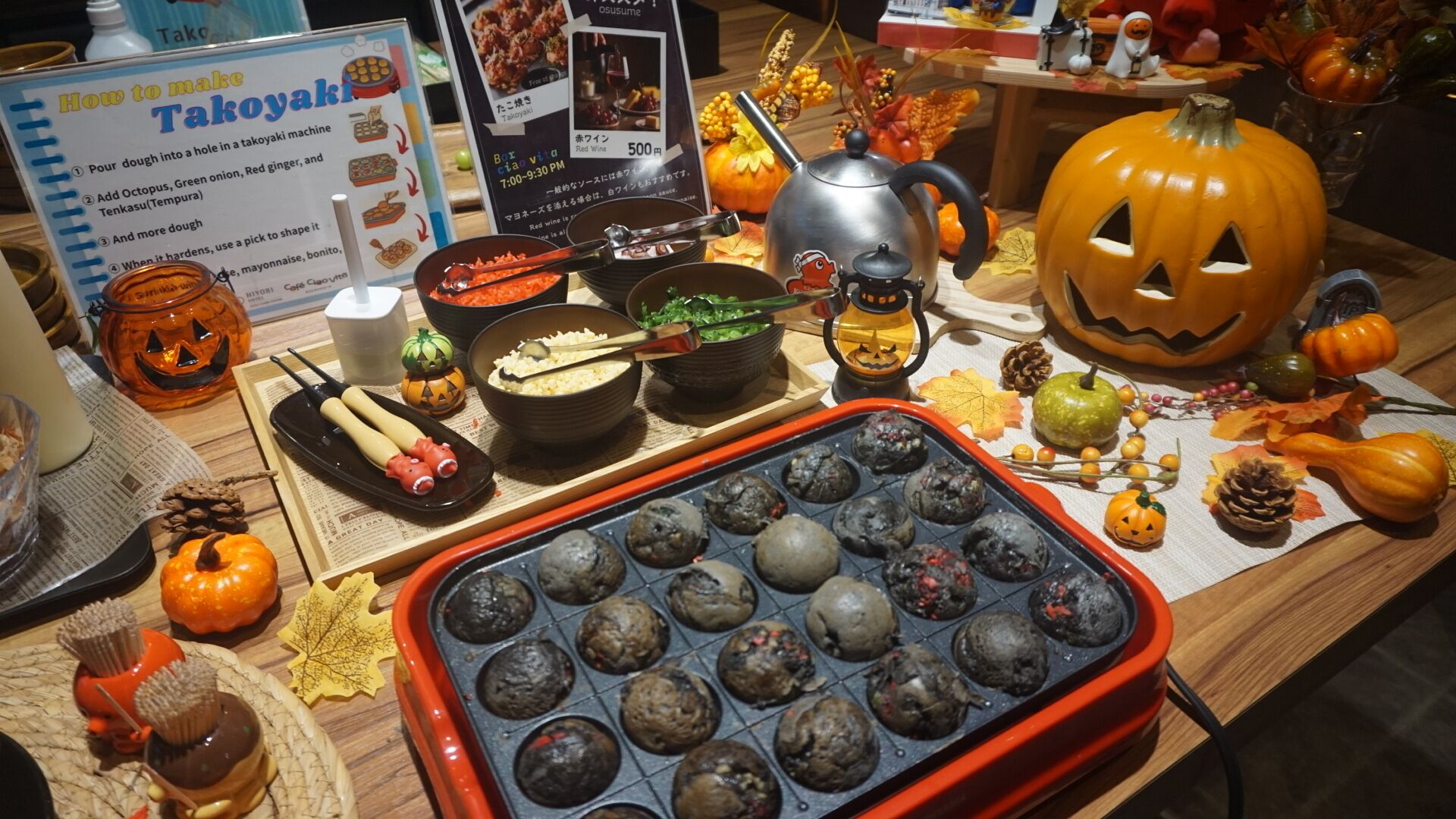 A food display with Takoyaki, a takoyaki machine, and a sign explaining how to make Takoyaki.