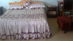 A bedroom with a bed, a chair, a nightstand, and a hanging mosquito net. - Serene Hotel (Mbarara)
