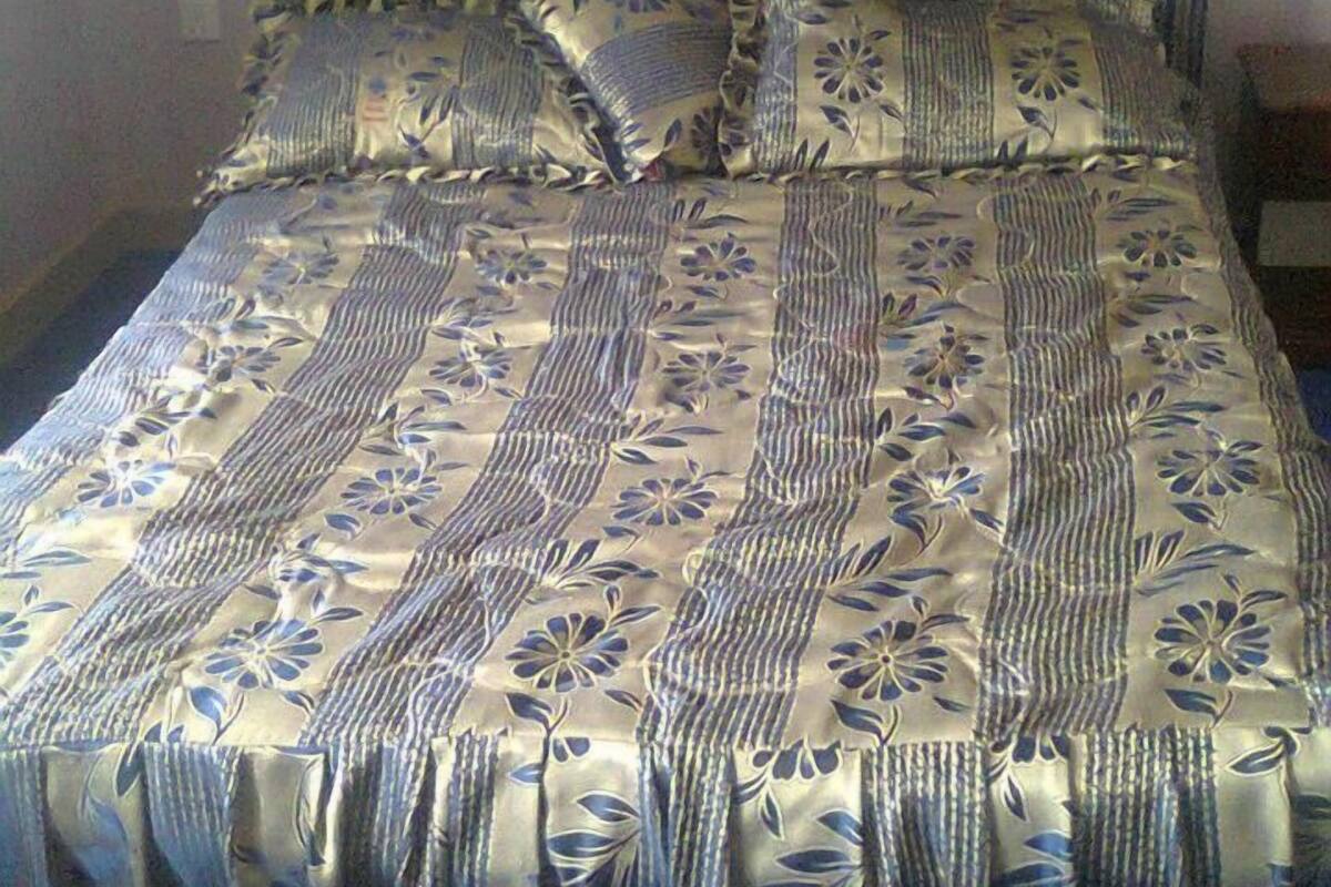 A bed with a striped and floral patterned bedspread, a matching pillow, and a headboard.