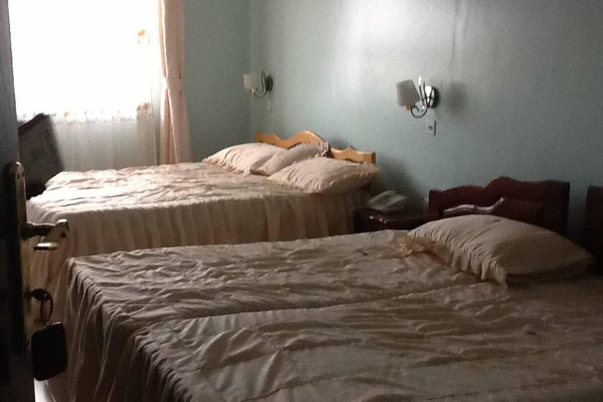 A room with two beds, a nightstand, a lamp, and a window with curtains.
