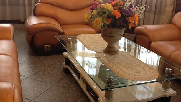 A living room with a glass coffee table, leather armchairs, and a vase with flowers. - Serene Hotel (Mbarara)