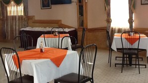 A dining area with tables set for four, each with a white tablecloth and orange runners. There are black chairs around the tables. - Serene Hotel (Mbarara)