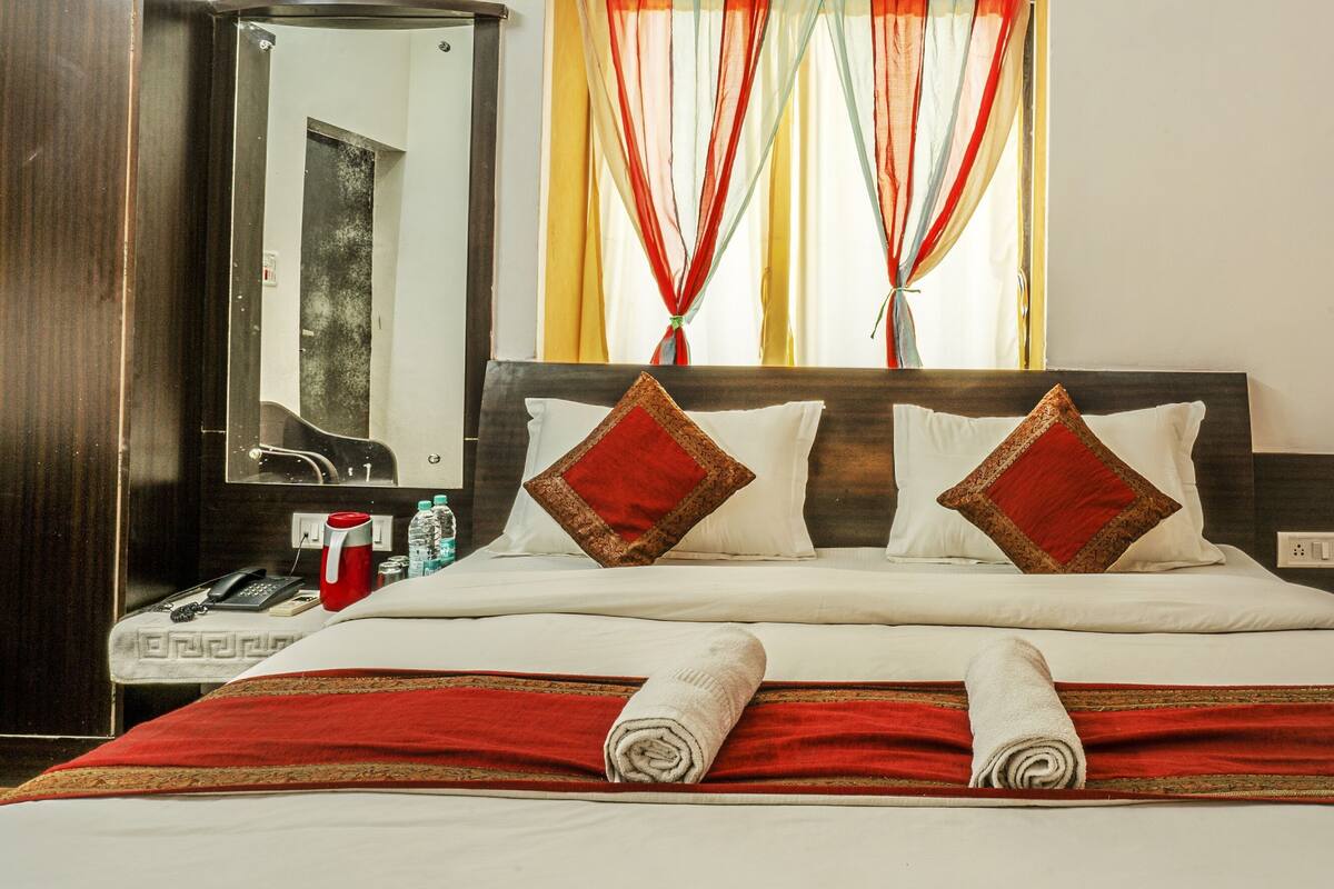 Une chambre d’hôtel avec un lit, un miroir, un téléphone, une bouteille d’eau et une couverture de lit rouge et blanche.