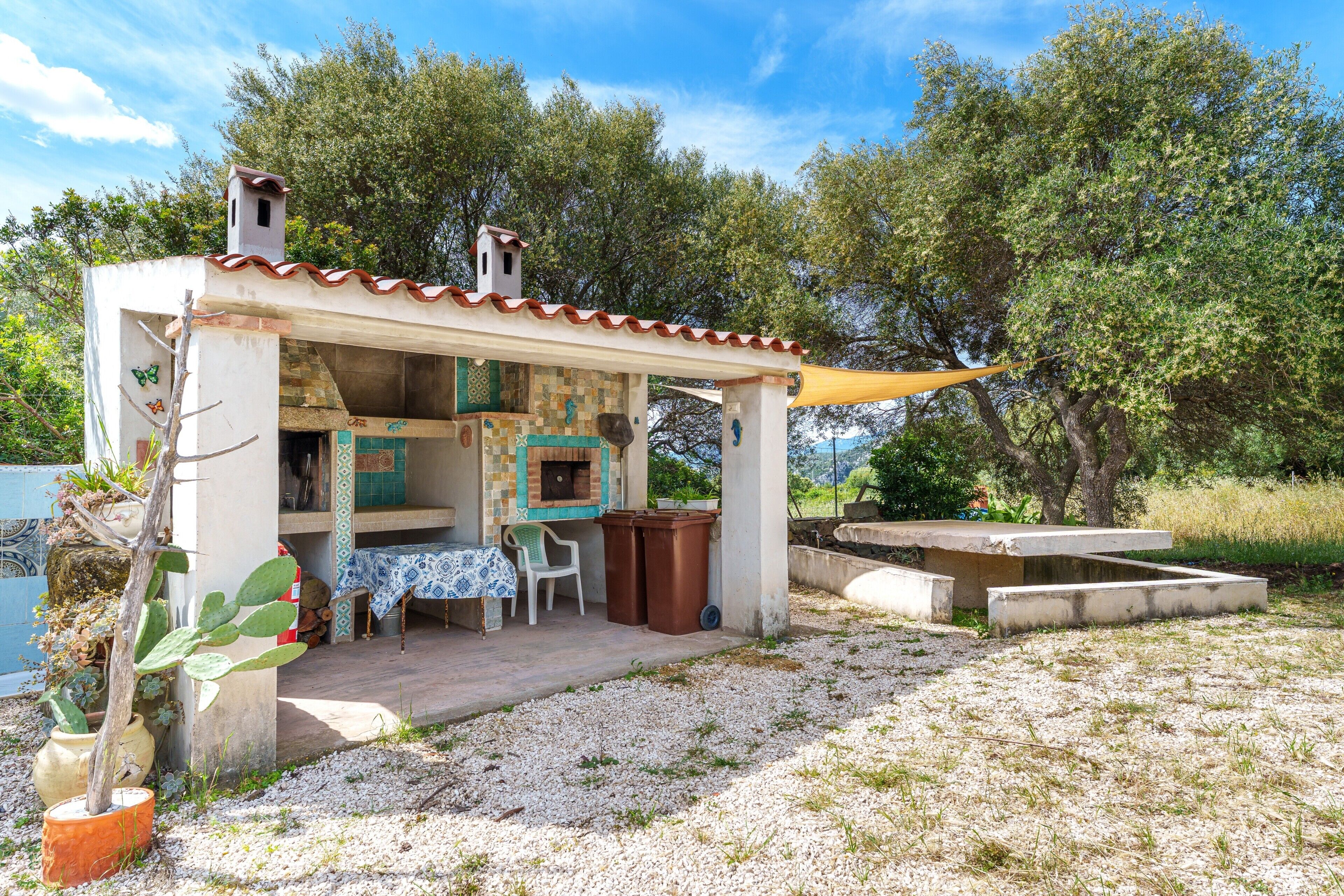 A small outdoor kitchen with a table and chairs, surrounded by trees.