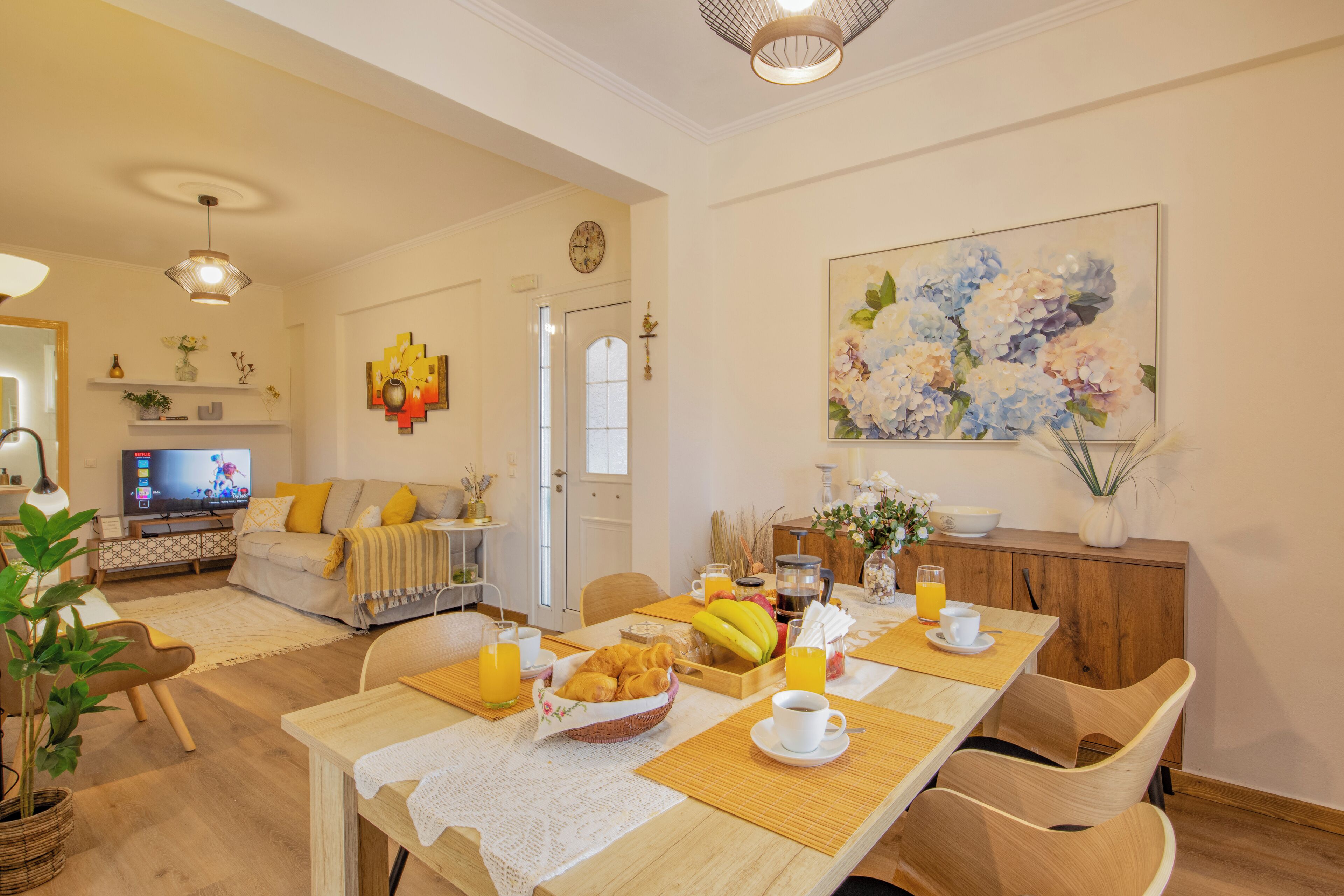 A dining area with a wooden table set for breakfast, including croissants, fruit, and beverages.