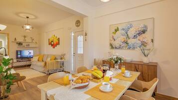 A dining area with a wooden table set for breakfast, including croissants, fruit, and beverages.