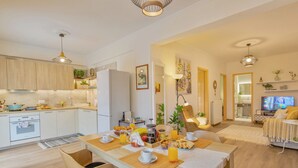 Eine moderne Küche mit Holzausstattung, ein Essbereich mit Frühstücksangebot und ein Wohnzimmer mit Fernseher.