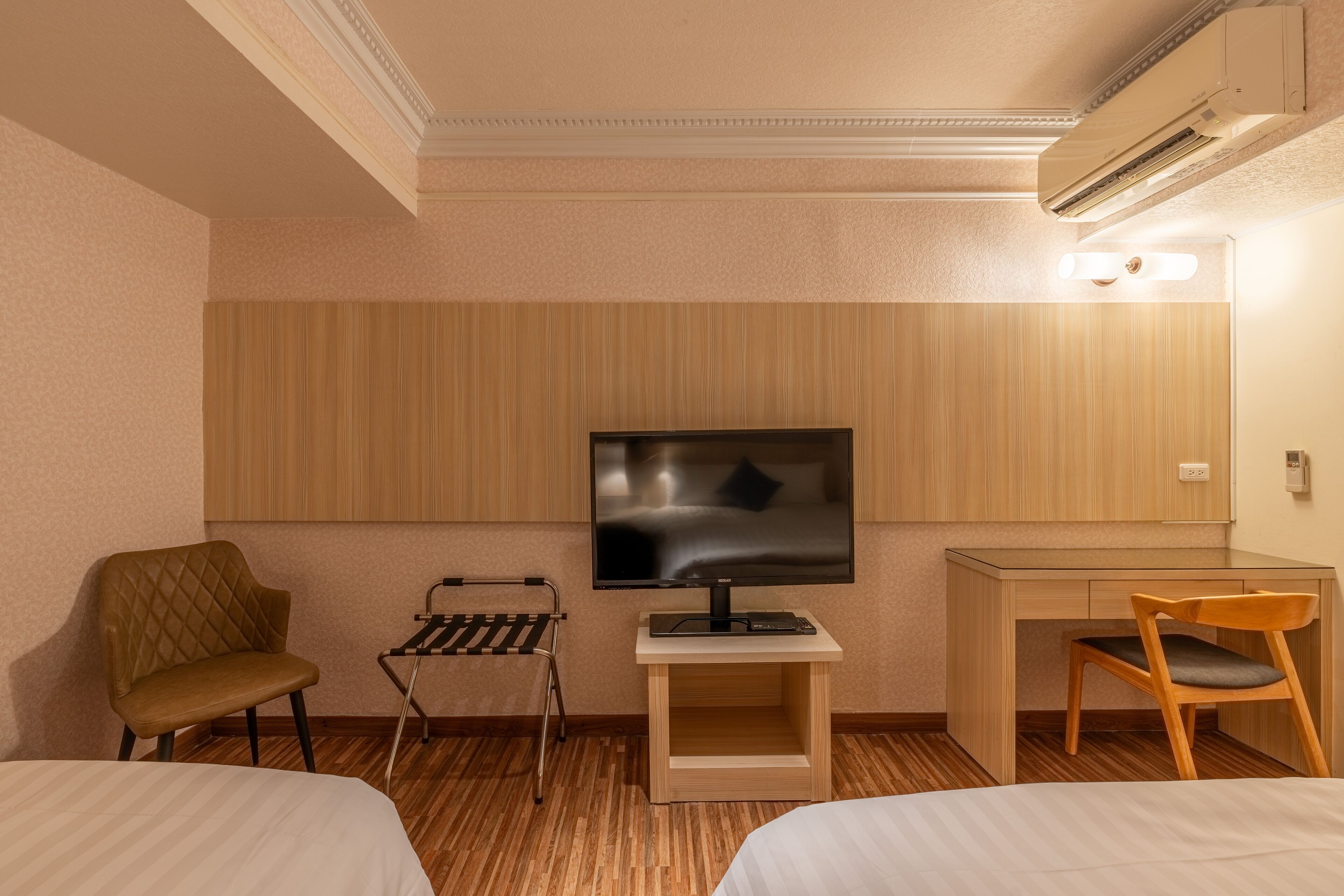 A hotel room with a bed, a desk, a chair, a TV, and a small table.