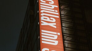 A vertical sign for Chillax Inn GO! with a geometric logo below it. - Chillax Inn (Kaohsiung)