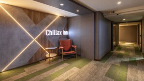 A hotel lobby with a 'Chillax Inn' sign, a red armchair, a small round table, and a patterned carpet. - Chillax Inn (Kaohsiung)
