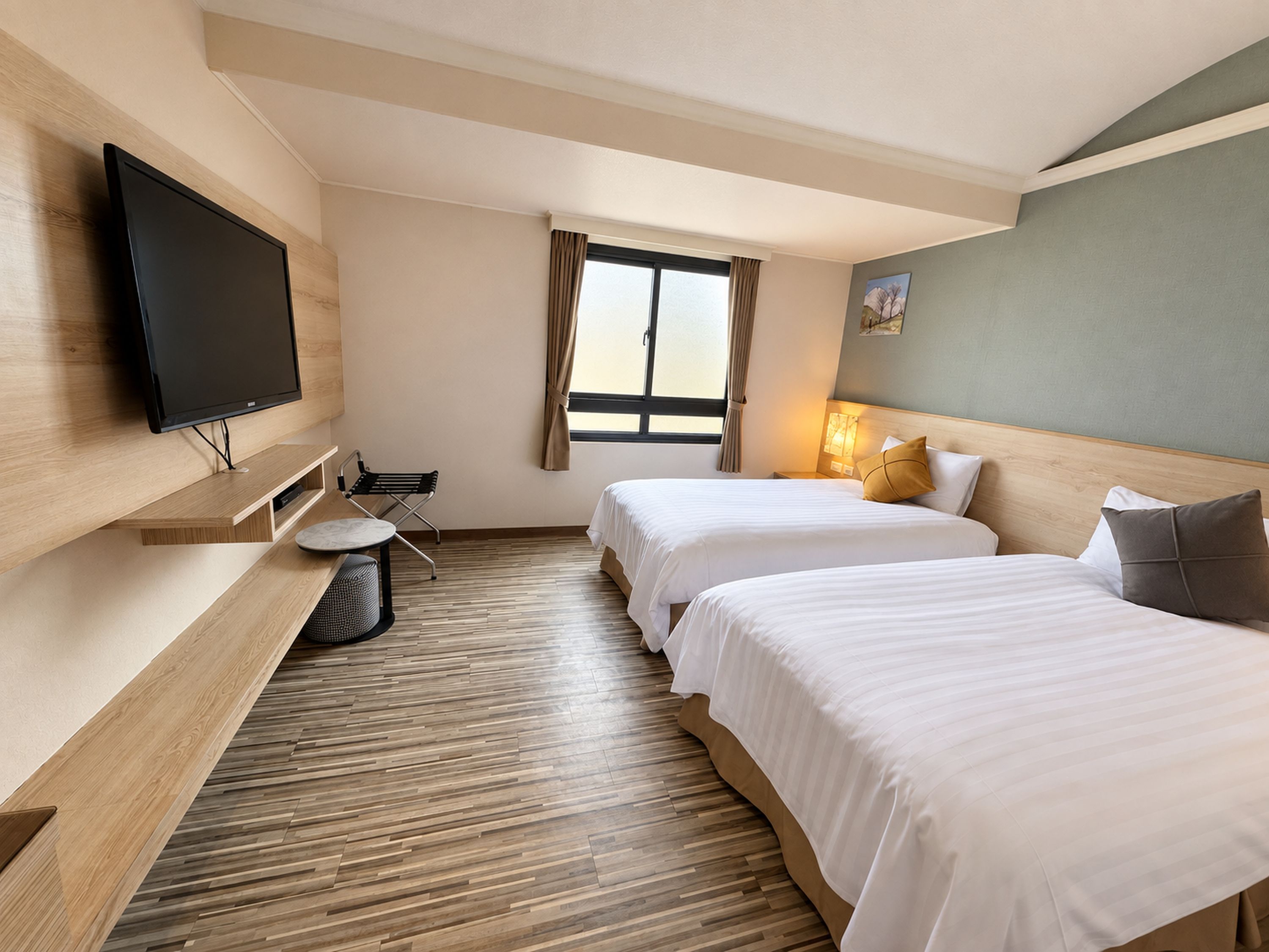 Une chambre d’hôtel avec deux lits, un téléviseur fixé au mur, une petite table et une fenêtre avec des rideaux.