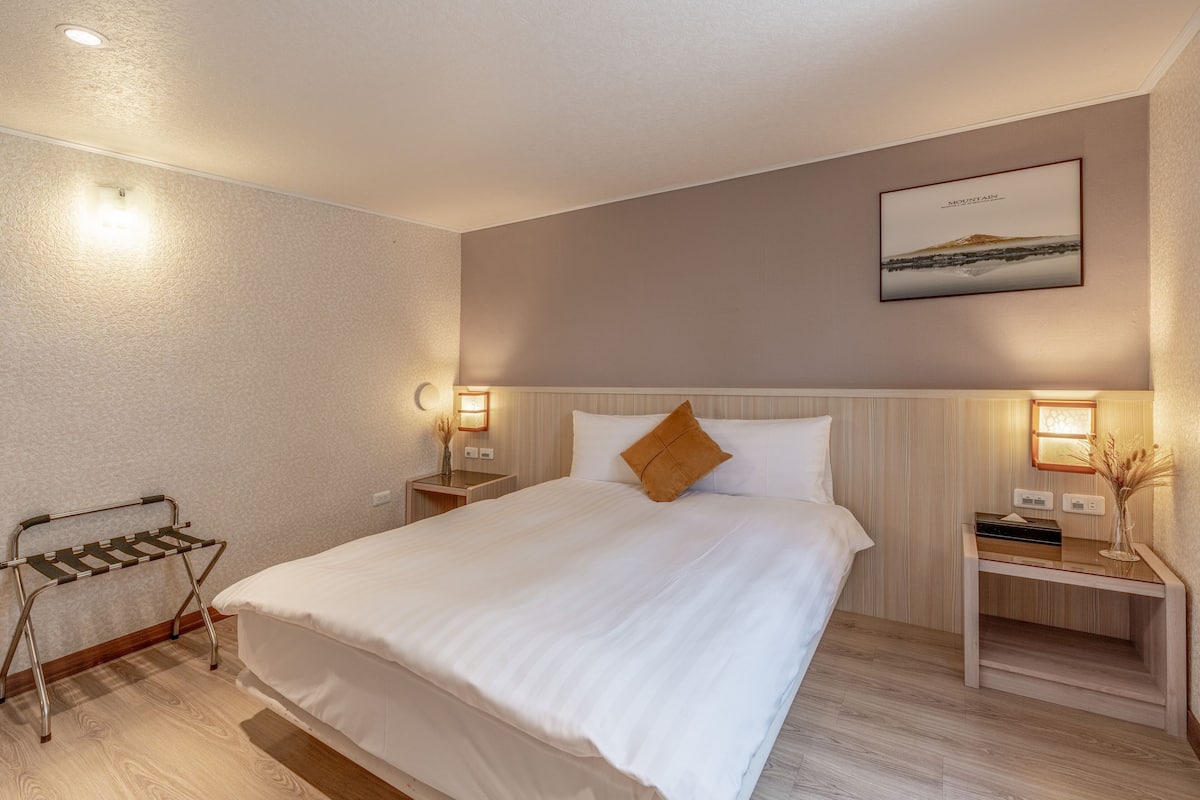 Un lit bien fait avec un seul oreiller, une table de chevet avec une lampe et un cadre photo fixé au mur.