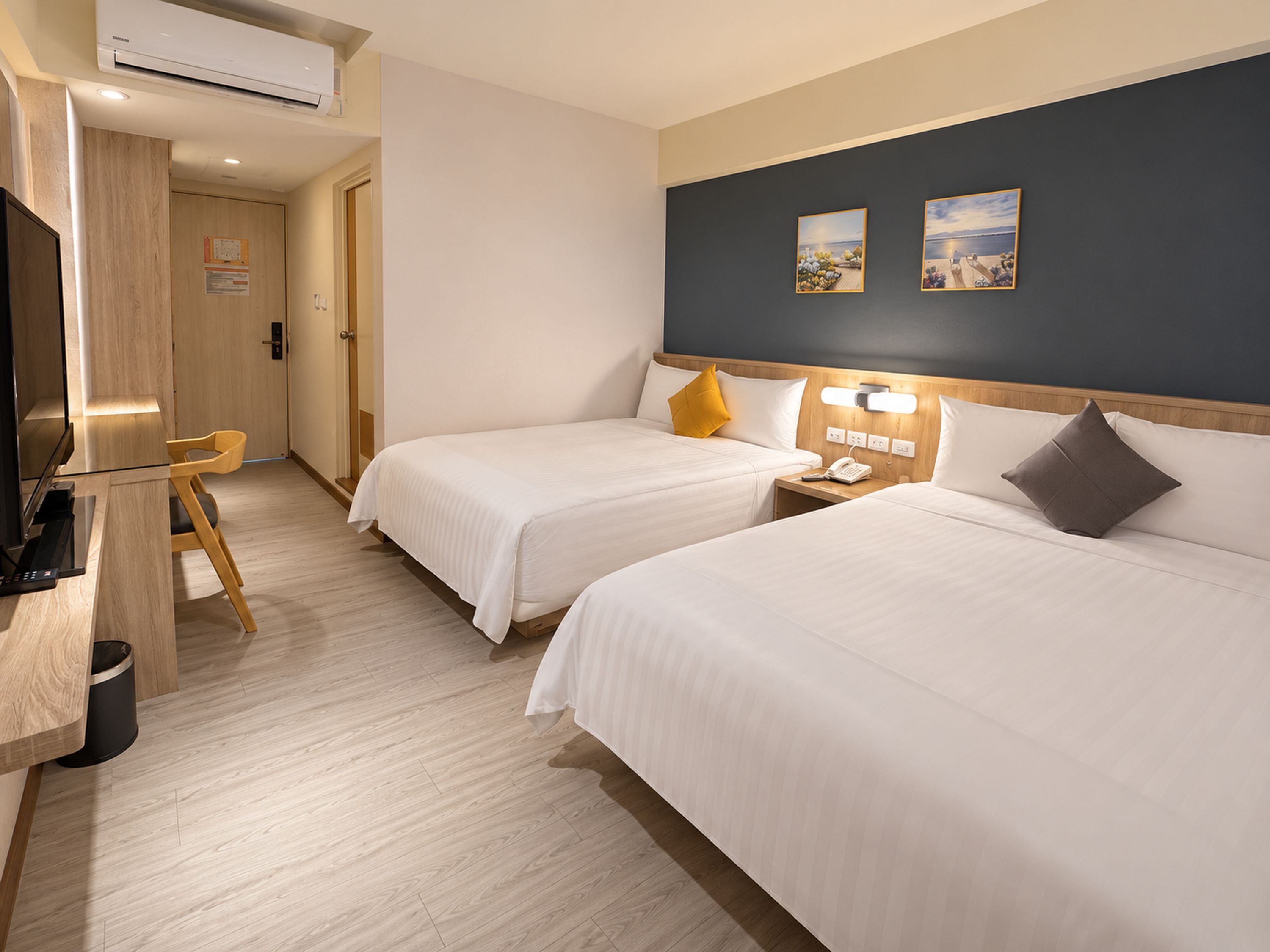 A hotel room with two beds, a desk, a chair, and a nightstand with a phone.
